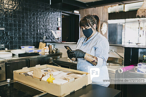 Weiblicher Koch  der ein Smartphone benutzt  während er an der Küchentheke eines Restaurants steht  in dem das Coronavirus grassiert.