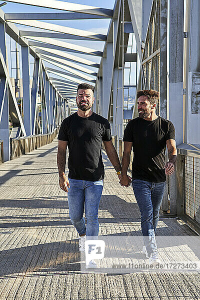 Happy homosexual couple holding hands while walking on bridge