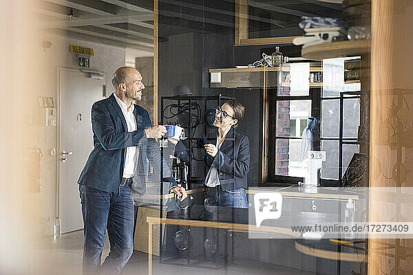 Lächelnde Geschäftsleute  die im Büro stehend eine Kaffeetasse rösten