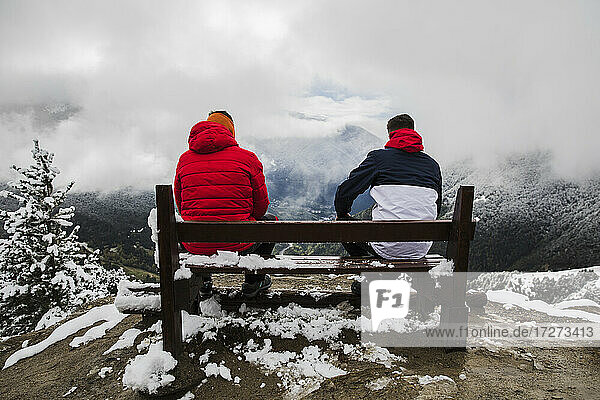 Male friends sitting on bench in mountain during winter
