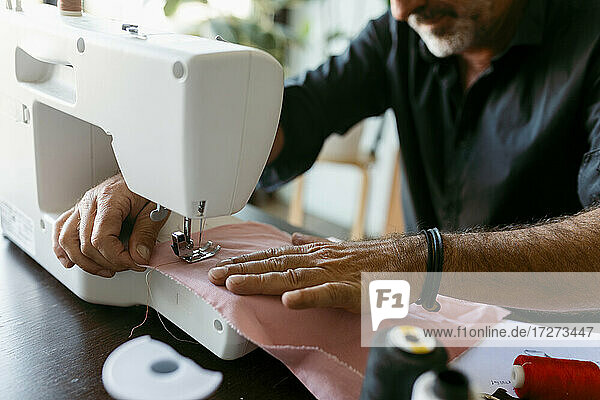 Male costume designer sewing fabric while working in studio