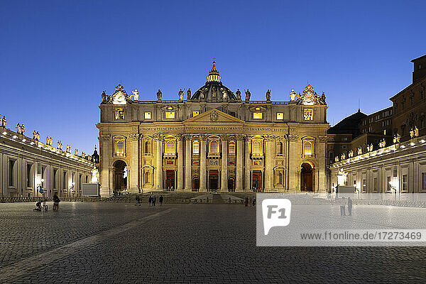 Beleuchtete Fassade des Petersdoms und des Petersplatzes gegen einen klaren blauen Himmel in der Abenddämmerung  Vatikanstadt  Rom  Italien