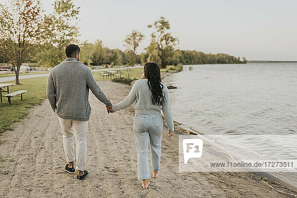 Couple holding hands while walking by lake