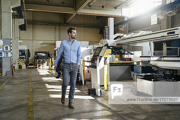 Junger Geschäftsmann hält Aktentasche beim Spaziergang in einer Fabrik