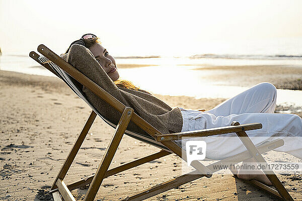 Schöne junge Frau entspannt sich auf einem Klappstuhl am Strand bei Sonnenuntergang