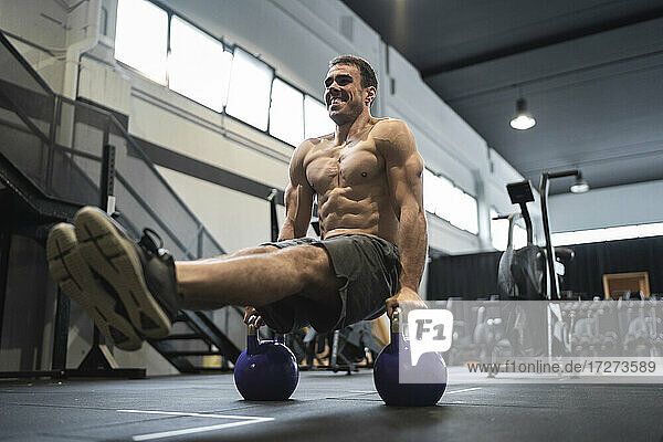 Smiling male athlete exercising with kettle bell in gym