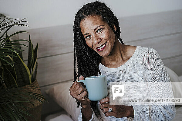Lächelnde reife Frau trinkt Kaffee  während sie zu Hause sitzt