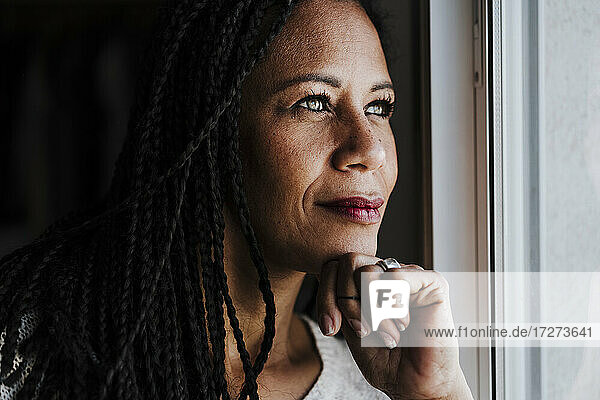 Mature Woman with hand on chin looking through window standing at home