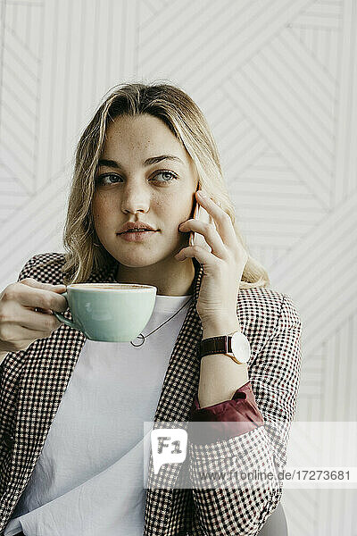 Junge Frau schaut weg  während sie in einem Café sitzt und Kaffee trinkt