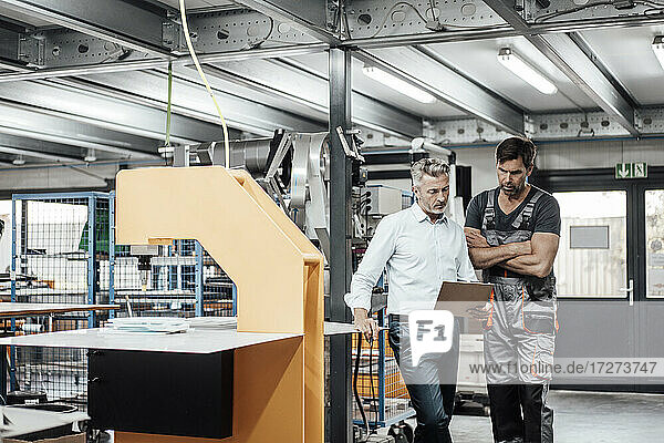 Männlicher Arbeiter und Manager diskutieren über ein Dokument  während sie in einer Fabrik stehen