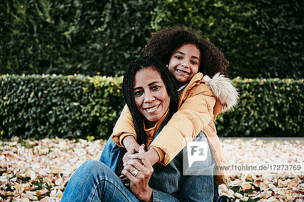 Smiling girl embracing mother from behind while sitting at park