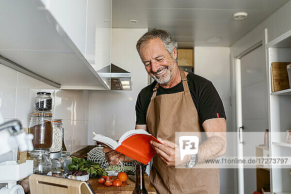 Älterer Mann lächelt beim Lesen eines Buches in der Küche zu Hause