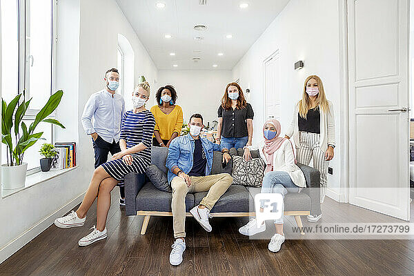 Employees wearing face mask standing and sitting by sofa at office