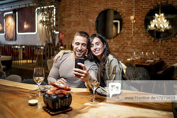 Lächelnde Freunde  die ein Selfie machen  während sie am Tisch im Restaurant sitzen