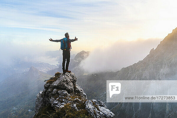 Pensive hiker with arms outstretched standing on mountain peak during sunrise at Bergamasque Alps  Italy
