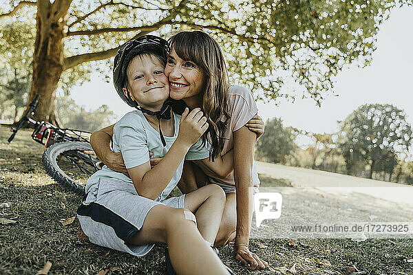 Mutter umarmt ihren Sohn in einem öffentlichen Park an einem sonnigen Tag