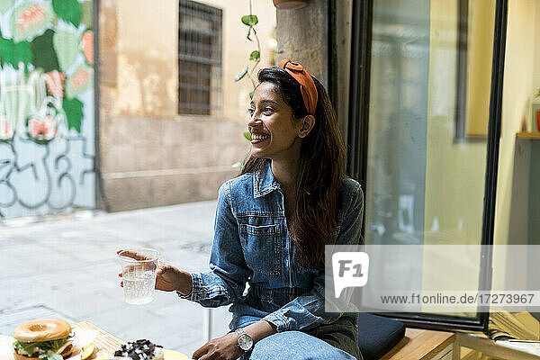 Lächelnde junge Frau  die in einem Café am Fenster sitzt und isst