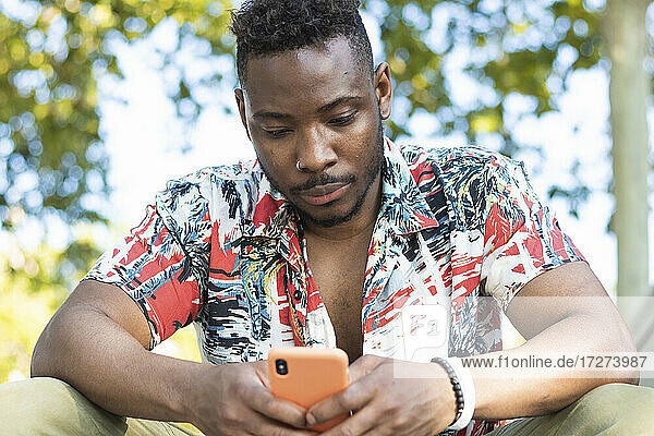 Junger Mann  der im Freien sitzend ein Smartphone benutzt