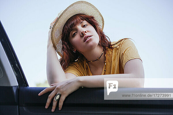 Beautiful young woman wearing hat leaning on car window