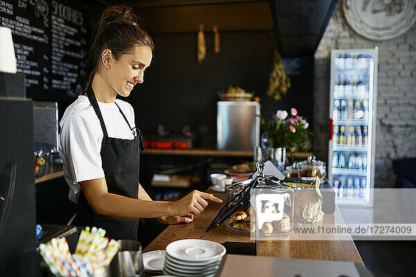 Lächelnder Barista mit digitalem Tablet an der Küchentheke eines Cafés
