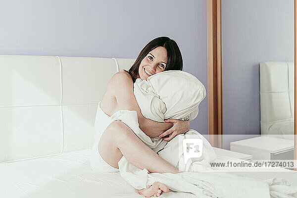 Glückliche schöne Frau umarmt Decke sitzt auf dem Bett zu Hause