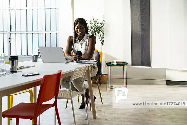 Lächelnde Geschäftsfrau  die ein Mobiltelefon benutzt  während sie am Schreibtisch im Büro sitzt