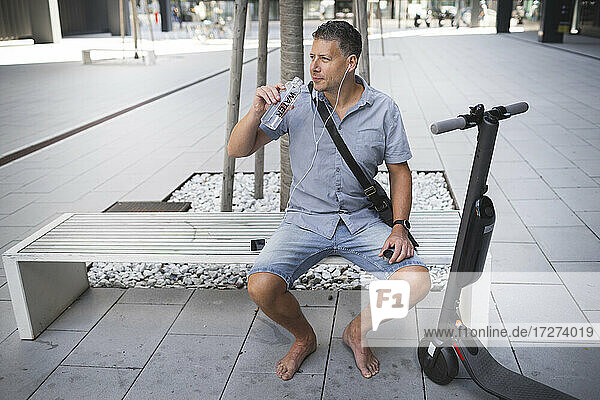 Mature man looking away while drinking water sitting on bench