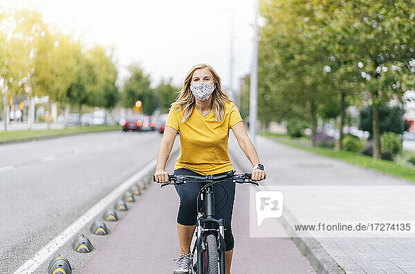Woman wearing protective face mask cycling on bicycle lane in city