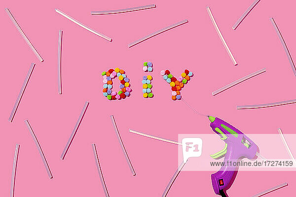DIY Text arrangiert mit bunten Pom Poms und Klebepistole auf rosa Hintergrund im Studio
