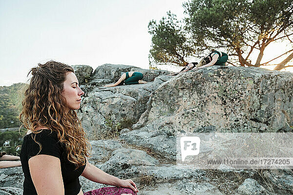 Frau meditiert mit Freundinnen auf Felsen vor klarem Himmel