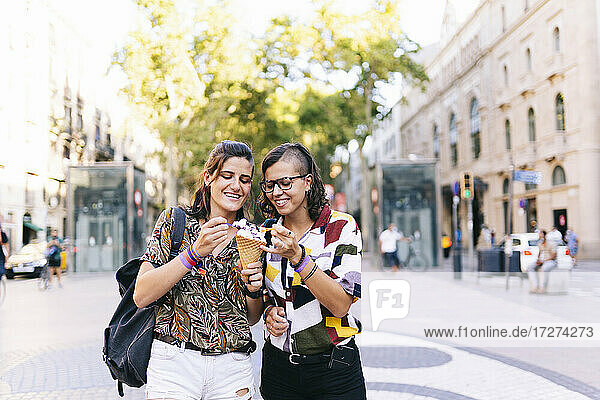 Lesbisches Paar isst Eis  während es auf der Straße in der Stadt steht