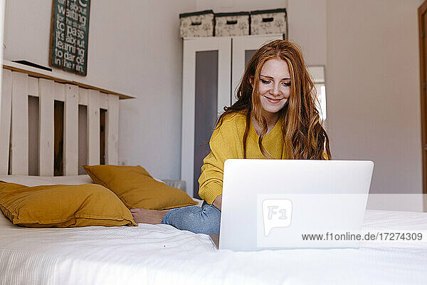 Junge Geschäftsfrau  die einen Laptop benutzt  während sie im Schlafzimmer zu Hause sitzt