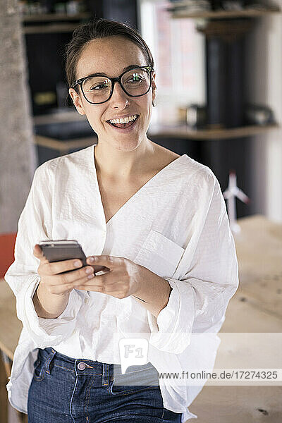 Geschäftsfrau lächelnd bei der Verwendung eines Mobiltelefons im Büro stehend