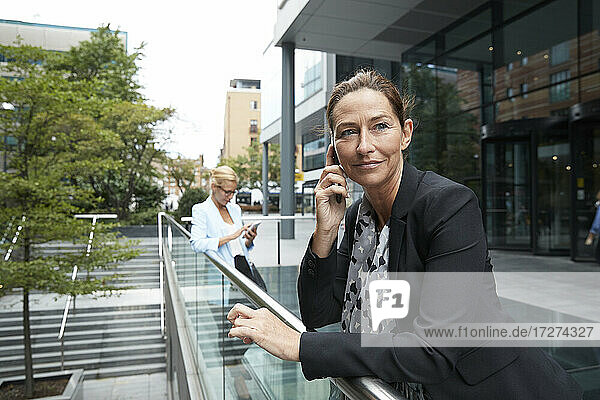 Woman talking on mobile phone while colleague standing in background at city