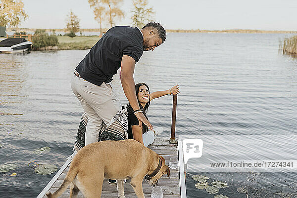 Mann steht mit Frau und Hund auf einem Steg am See