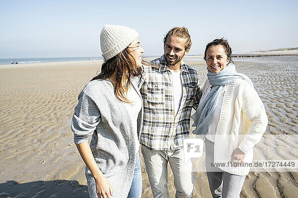 Lächelndes Paar und Mutter  die mit dem Arm am Strand spazieren gehen