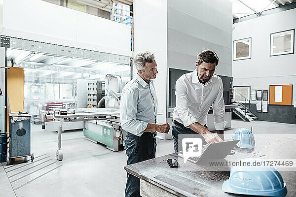 Male engineer pointing while discussing over laptop with colleague in manufacturing industry