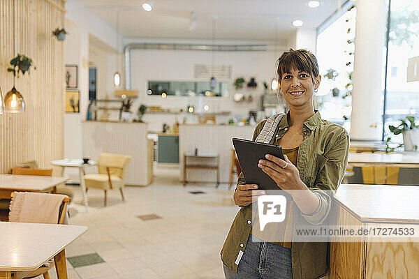 Lächelnde Besitzerin mit digitalem Tablet in einem Café stehend