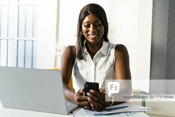Junge Frau  die ein Mobiltelefon benutzt  während sie am Schreibtisch im Büro sitzt