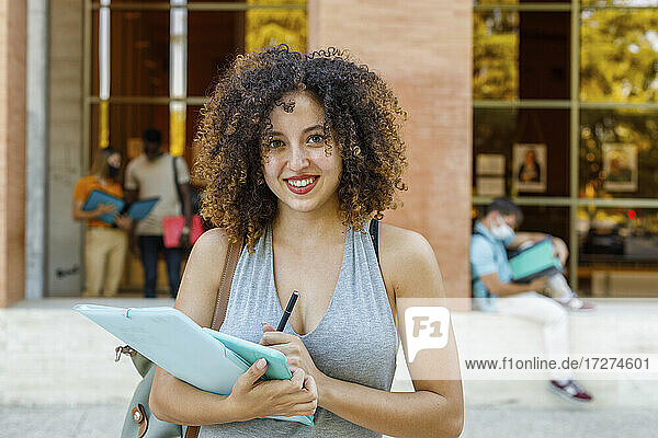 Junge lächelnde Frau mit Dokumenten auf einem Universitätscampus