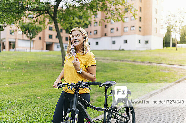 Lächelnde Frau mit Fahrrad auf dem Fußweg in der Stadt während COVID-19