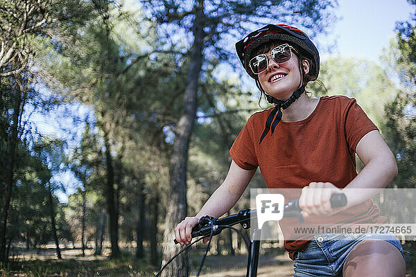 Happy young woman riding bicycle against trees at countryside
