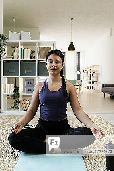 Junge Frau meditiert  während sie zu Hause auf einer Übungsmatte sitzt