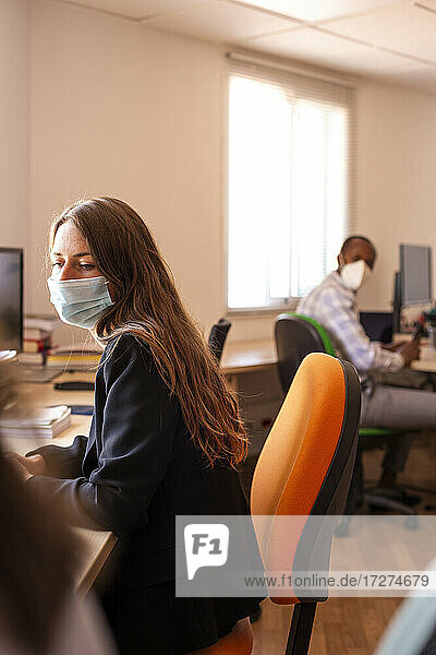 Businesswoman in protective face mask working at desk in office