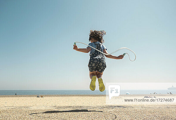 Mädchen spielt mit Springseil und springt am Strand gegen den klaren Himmel