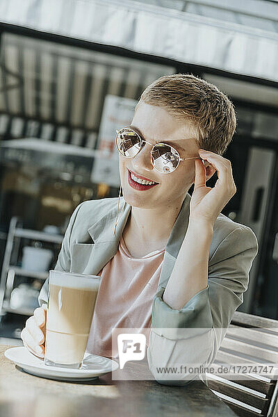 Mittlere erwachsene Frau mit Sonnenbrille und Kaffeeglas in einem Straßencafé an einem sonnigen Tag
