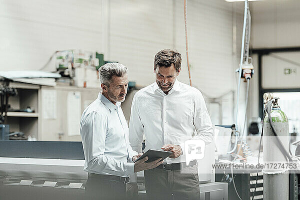Mature male engineers discussing over digital tablet while standing in manufacturing industry