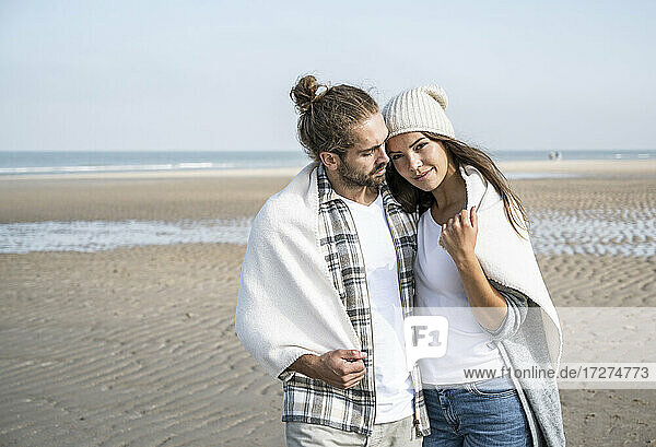 Junges  in eine Decke gehülltes Paar  das am Wochenende seine Freizeit am Strand verbringt