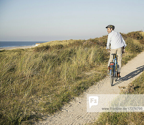 Happy man looking at view while riding bicycle on beach against clear sky