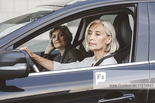 Geschäftsfrau sitzt mit einem Kollegen am Steuer eines Autos in der Stadt